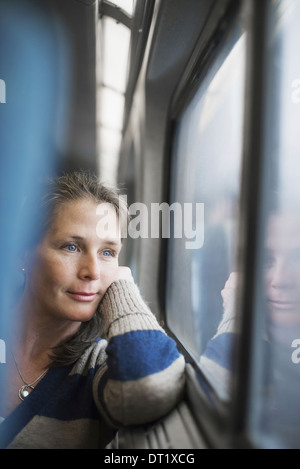 Une femme assise sur un siège côté fenêtre dans un train transport posant sa tête sur sa main à la recherche dans la distance Banque D'Images