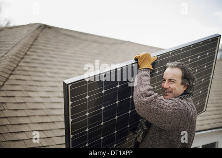 Un homme portant un grand panneau solaire à l'échelle d'une ferme Banque D'Images