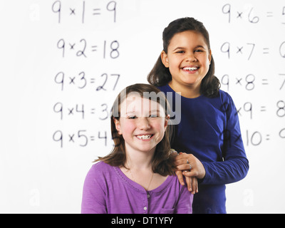 Deux jeunes filles à la recherche lors d'une série de tables de multiplication mathématique sur un mur clair voir au travers de l'apprentissage avec un stylo noir Banque D'Images