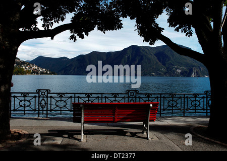 Un banc rouge entre deux arbres devant le lac de Lugano Banque D'Images