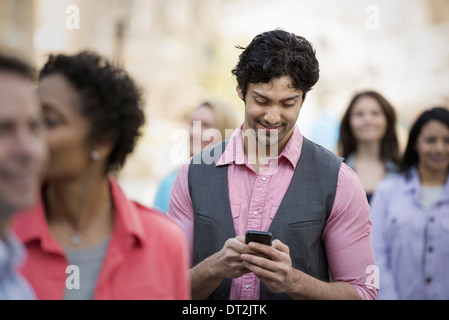 Les gens à l'extérieur dans la ville au printemps un homme regardant son téléphone cellulaire Banque D'Images