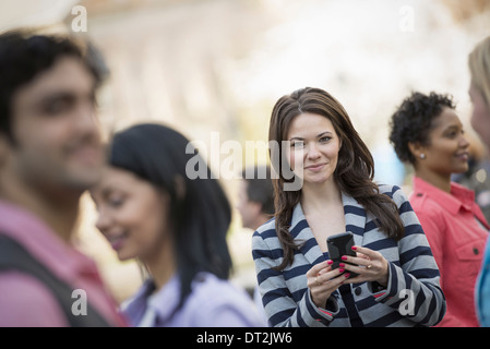 Park a young woman holding a mobile phone et à la recherche jusqu'à l'appareil photo Banque D'Images