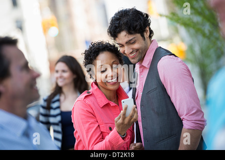 Les gens à l'extérieur au printemps New York City park quatre personnes hommes et femmes à un couple à la recherche d'un écran de téléphone mobile Banque D'Images