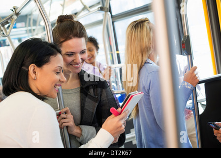 Les gens de la ville de New York les hommes et les femmes sur un autobus de ville transports publics deux femmes à la recherche d'une tablette numérique à l'ordinateur de poche Banque D'Images