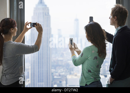 Mode de vie urbain trois personnes debout sur une plate-forme d'observation à l'aide de leurs téléphones portables pour prendre des images de la vue sur la ville Banque D'Images