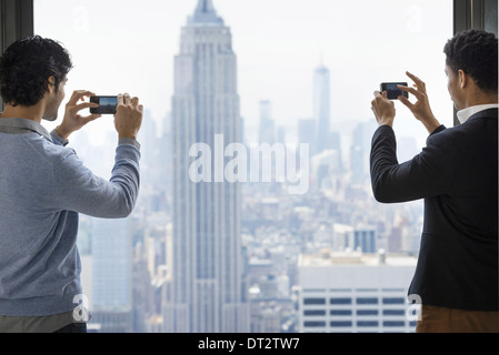 Deux jeunes hommes à l'aide de leurs téléphones portables pour prendre des images de la ville à partir de la plate-forme d'observation avec vue sur l'Empire State Building Banque D'Images