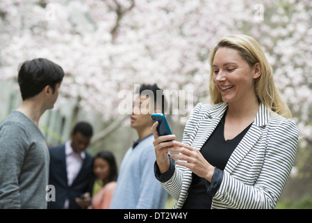 Vue sur cityA femme en utilisant son téléphone cellulaire et d'un groupe de quatre personnes, hommes et femmes dans l'arrière-plan Banque D'Images