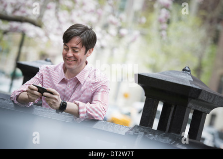 Vue sur cityA homme assis à l'extérieur dans un parc de la ville en regardant son smart phone and smiling Banque D'Images