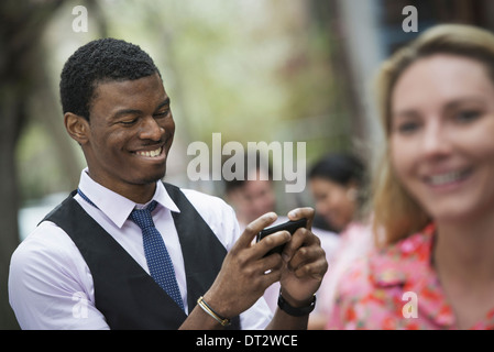 Vue sur un parc, un homme cityin sourire comme il regarde son téléphone et d'un proche d'un maximum d'une femme aux cheveux blonds Banque D'Images