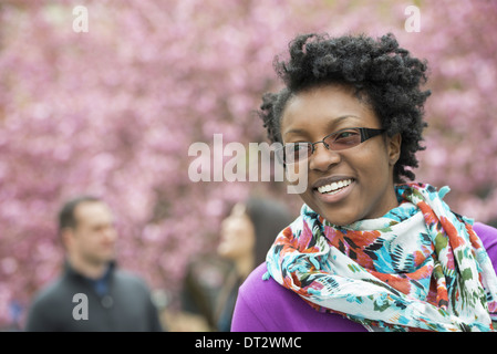Un groupe de personnes sous l'cerisiers dans le parc A young woman smiling portant une chemise violette et foulard floral Banque D'Images