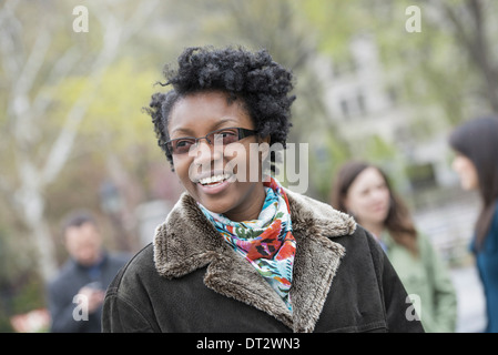 Un groupe de personnes dans un parc de la ville une jeune femme dans un manteau avec un col large sourire et regardant la caméra Banque D'Images