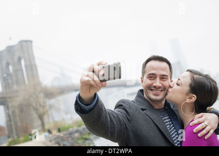 Passage sur le pont de Brooklyn, l'East River, un couple de prendre une photo avec un téléphone un selfy d'eux-mêmes Banque D'Images