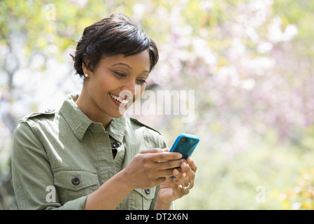 Soleil et cherry blossom une femme contrôle de son smart phone Banque D'Images