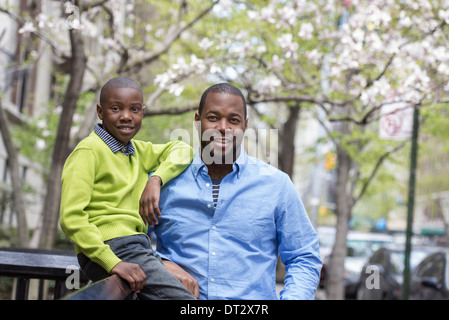 Soleil et fleur de cerisier Un garçon assis sur une barrière à côté de son père Banque D'Images