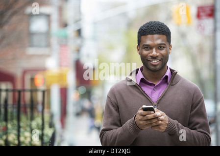 Un jeune homme tenant son téléphone et smiling at the camera Banque D'Images