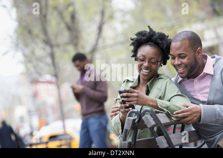 Une femme et un homme sur un banc, contrôler son téléphone deux hommes dans l'arrière-plan Banque D'Images