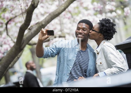 Une femme s'embrasser un homme et de prendre une photo avec un téléphone mobile de poche Banque D'Images