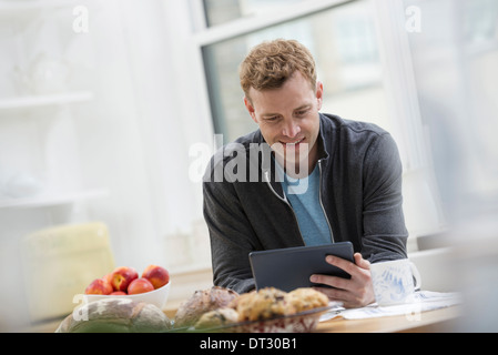 Un bureau ou un appartement à New York de l'intérieur un homme dans un sweat-shirt top en utilisant une tablette numérique s'appuyant sur un bar de petit-déjeuner Banque D'Images