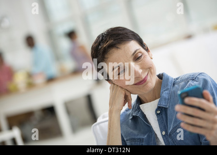 Une femme mature aux cheveux gris portant une chemise en jean à la recherche à l'écran d'un téléphone intelligent Banque D'Images