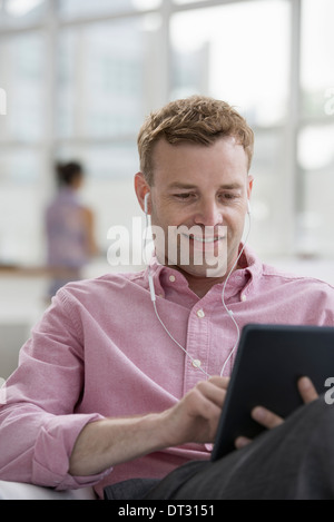 Un homme en chemise rose sitting smiling using a digital tablet Banque D'Images