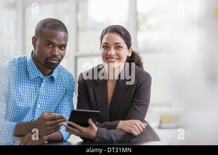Professionnels à l'office un cadre lumineux et spacieux lieu de travail Deux personnes assis à un bureau à l'aide d'une tablette numérique, les collègues de travail Banque D'Images