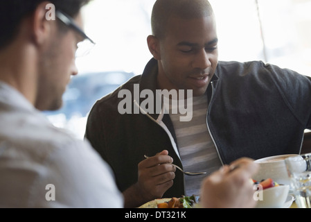 Deux hommes assis à une table de café ayant un repas Banque D'Images