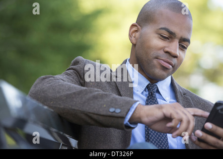 Un homme assis sur un banc de contrôle de son téléphone cellulaire Banque D'Images