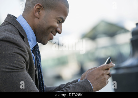 Un homme assis sur un banc de contrôle de son smart phone Banque D'Images