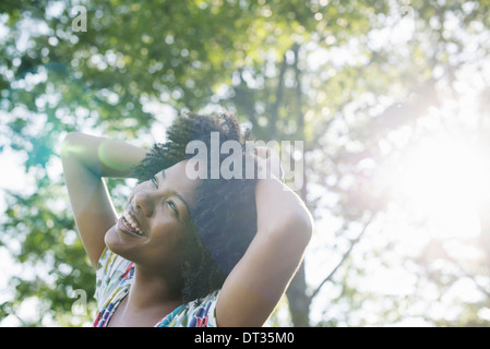 Une jeune femme en robe d'été fleurie avec ses mains derrière sa tête en souriant et regardant vers le haut Banque D'Images