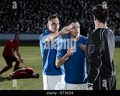 Joueurs de football se disputer avec arbitre sur terrain Banque D'Images