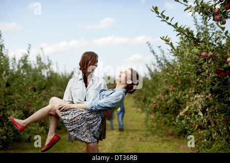 Lignes d'arbres fruitiers dans un verger bio deux jeunes femmes riant l'un portant l'autre Banque D'Images