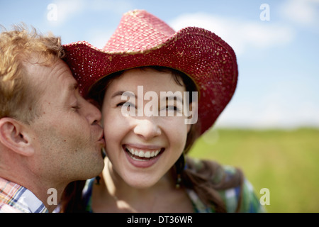 Une jeune femme en rose à larges bords chapeau d'être embrassé sur la joue par un jeune homme Banque D'Images