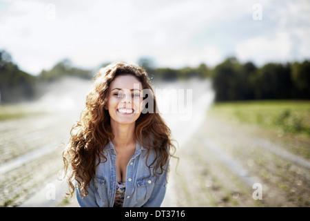 Une jeune femme en veste en jean debout dans un champ de travail sprinkleurs irrigation dans l'arrière-plan Banque D'Images