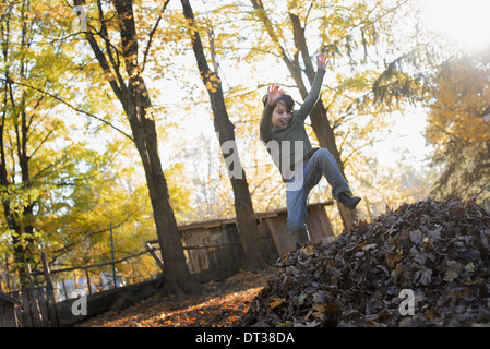 Un enfant à l'automne le soleil dans un bois. Sauter dans un grand tas de feuilles d'automne jusqu'ratissée. Banque D'Images