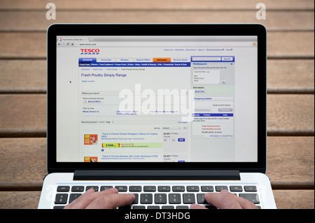 Le site web de Tesco sur un MacBook contre un banc en bois fond de plein air y compris les doigts d'un homme (usage éditorial uniquement). Banque D'Images