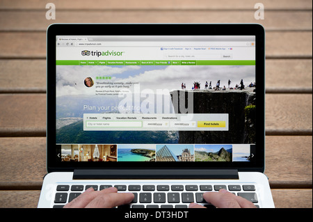 Le site internet Trip Advisor sur un MacBook contre un banc en bois fond de plein air y compris les doigts d'un homme (usage éditorial uniquement). Banque D'Images