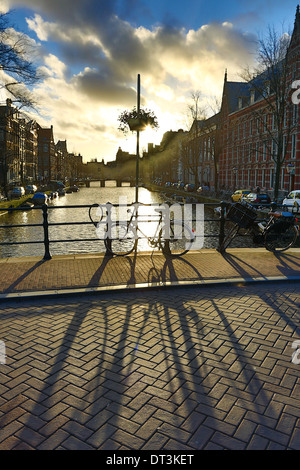 Silhouette d'un vélo en stationnement et son ombre sur un pont au-dessus d'un canal au coucher du soleil à Amsterdam, Hollande Banque D'Images