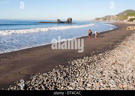 Un couple de surfers promenade sur la plage après le début de séance du matin El Tunco, une ville balnéaire en El Salvador très prisée des surfeurs. Banque D'Images