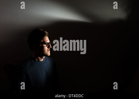 Un jeune homme portant des lunettes et photographié sur noir avec un arbre de lumière flash semble loin de caméra et du cadre. Banque D'Images