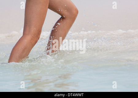 Les jambes d'une femme marchant dans l'eau sur une plage Banque D'Images