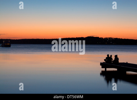 La silhouette de la famille assis sur fin de Warners Bay jetty at sunset Lake Macquarie NSW Australie Nouvelle Galles du Sud Banque D'Images