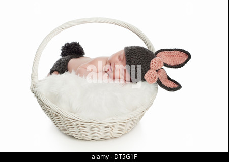 Sourire petite fille dormir dans un panier et portant un costume de lapin. Banque D'Images