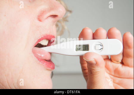 Femme de prendre sa propre température en utilisant un thermomètre numérique Banque D'Images