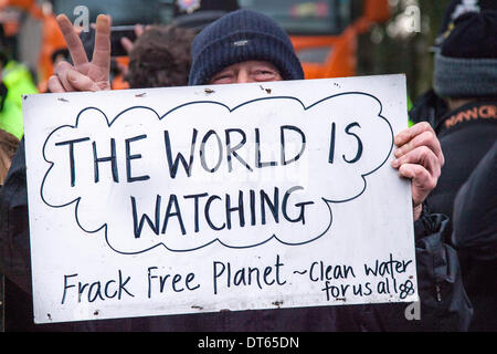 Barton Moss, Manchester, Royaume-Uni. 10 fév, 2014. ' Le monde regarde' et 'les signes de fracturation Planet' manifestations anti-bannière par fracturation militants contre l'extraction du gaz de schiste, comme une opération de police par Greater Manchester Police continue au site de forage de l'IGAS à Barton Moss. Les manifestants cherchent à retarder et entraver la livraison des véhicules et des équipements de forage, en route vers le site d'exploration de gaz controversés. Les manifestants de fracturation ont mis en place un camp à Barton Moss Road, Eccles un potentiel d'extraction de gaz méthane-site à Salford, Greater Manchester. Banque D'Images