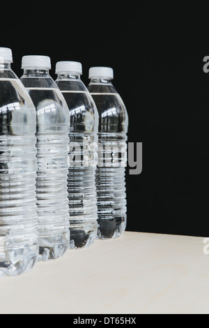 Rangée de clair, bouteilles d'eau en plastique rempli d'eau filtrée à la suite. sur un fond noir. Banque D'Images