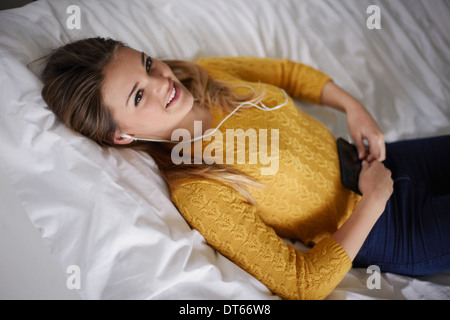 Portrait of teenage girl lying on bed listening to earphones Banque D'Images