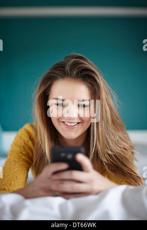 Teenage girl in bedroom texting on smartphone Banque D'Images