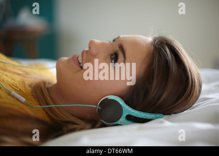 Portrait of teenage girl lying on bed listening to headphones Banque D'Images