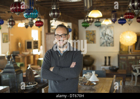 Un homme debout dans un magasin plein de meubles anciens et objets de décoration. Antique Shop s'affiche. L'éclairage, les nuances de verre et de meubles. Banque D'Images