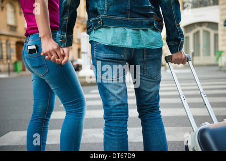 Jeune couple au croisement avec valise à roulettes, Paris, France Banque D'Images